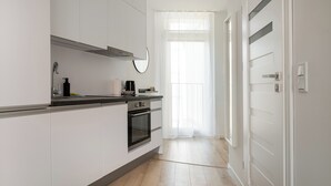 Uma cozinha moderna com armários brancos, coifa de aço inoxidável e uma janela com cortinas leves.