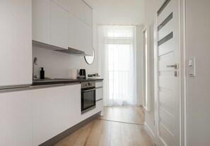A modern kitchen with white cabinetry, a stainless steel range hood, and a window with sheer curtains. - Browary Warszawskie Harmony Studio (Warszawa)