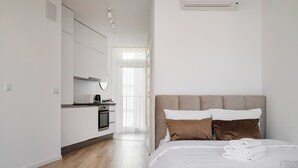 Quarto de hotel moderno com cama, cozinha compacta e vista para o exterior.
