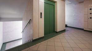 Un pasillo con un ascensor verde, paredes color beige y suelo de baldosas.