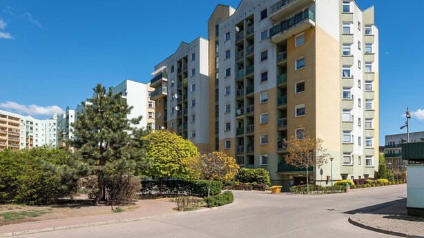 Un edificio residencial de varios pisos con balcones, cielo despejado y vegetación circundante.