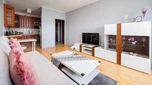 Una sala de estar moderna con sofá, mesa de centro, televisor y una cocina al fondo.