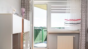 Una habitación con ventana, un radiador y vistas a una valla verde.