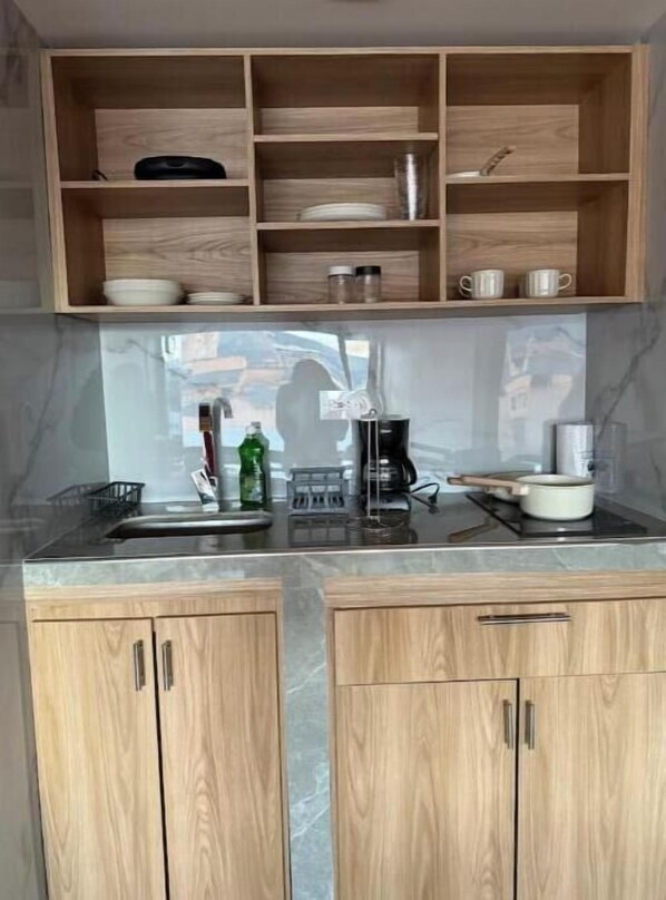 A kitchen with wooden cabinets, a marble countertop, and a wooden shelf above.