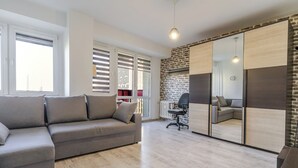 A modern living room with a grey sofa, a black office chair, a large mirror, and a brick wall. - Spodek Comfort Studio (Katowice)