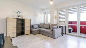 A modern living room with a sectional sofa, a wooden cabinet, and a large window with blinds. - Spodek Comfort Studio (Katowice)