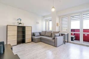 A modern living room with a sectional sofa, a wooden cabinet, and a large window with blinds. - Spodek Comfort Studio (Katowice)
