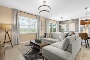 A modern living room with a sectional sofa, a coffee table, a lamp, and a view of the outside. - 8BR Themed Villa|Pool|Theater|RecRoom|Pet Friendly - Holiday Home (Kissimmee)