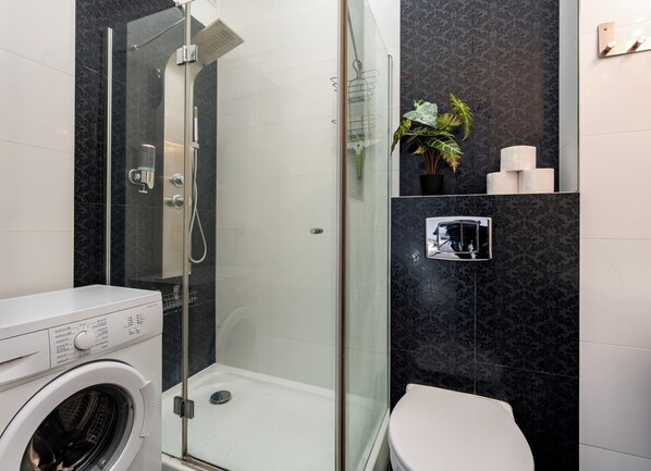 A modern bathroom with a glass-enclosed shower, a white toilet, and a washing machine.