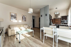 A modern living room with a sofa, a glass coffee table, and a dining area with chairs. - Officers Quarters Apartment (Gdynia)