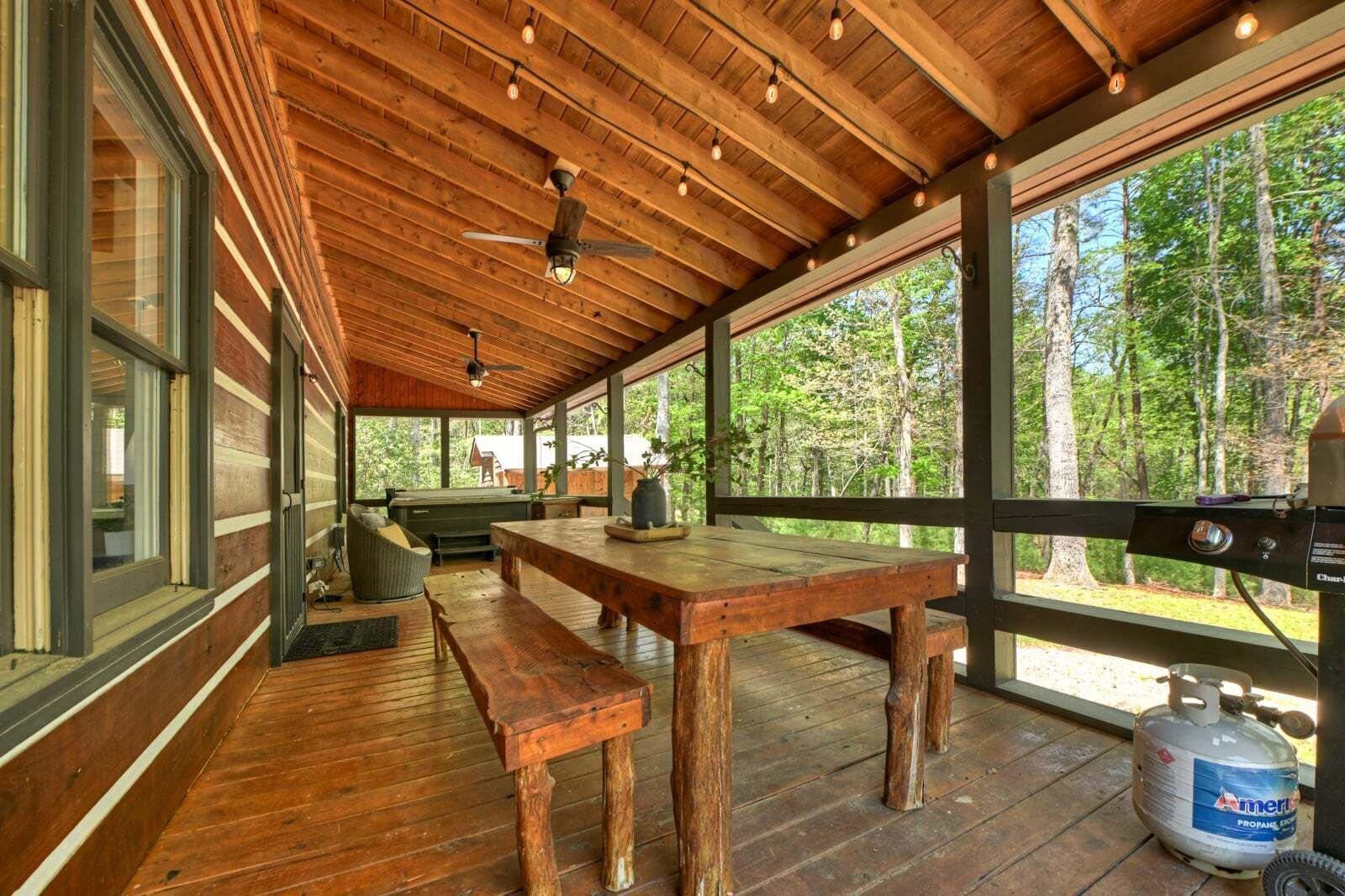 A wooden deck with a table and benches, large windows, and a propane tank.