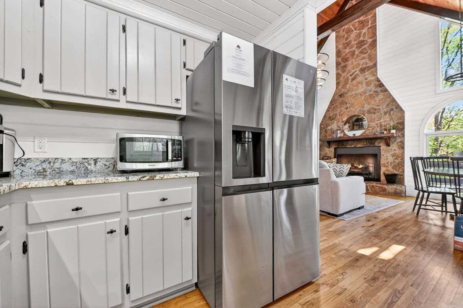 Una cocina con armarios blancos, un refrigerador de acero inoxidable, un microondas y una chimenea de piedra.