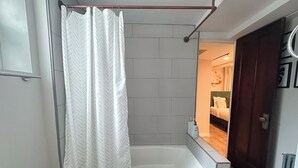 Un baño moderno con ducha, bañera y una puerta visible que da a otra habitación.