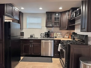 A modern kitchen with dark wood cabinets, stainless steel appliances, and a black countertop. - Studio Near Wrigley • Sleeps 4 • Games + Fireplace (Chicago)