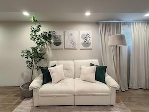 A living room with a white sofa, green cushions, a potted plant, and framed artwork on the wall. - Studio Near Wrigley • Sleeps 4 • Games + Fireplace (Chicago)