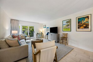 Un salon comprenant un canapé, des fauteuils, un téléviseur et des œuvres d’art accrochées aux murs.