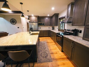 A modern kitchen with dark wood cabinets, stainless steel appliances, and a marble countertop. - Relax at Tees, Trees & Skis: a 4-bedroom retreat with hot tub and golf views on Mountaintop. (McHenry)