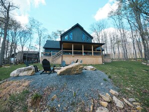 A two-story wooden cabin with a balcony, surrounded by a gravel path and large rocks. - Relax at Tees, Trees & Skis: a 4-bedroom retreat with hot tub and golf views on Mountaintop. (McHenry)