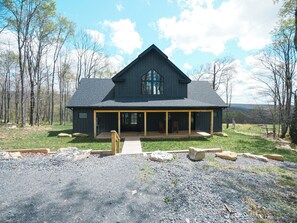 A large, dark wooden house with a covered porch and a gravel driveway. - Relax at Tees, Trees & Skis: a 4-bedroom retreat with hot tub and golf views on Mountaintop. (McHenry)