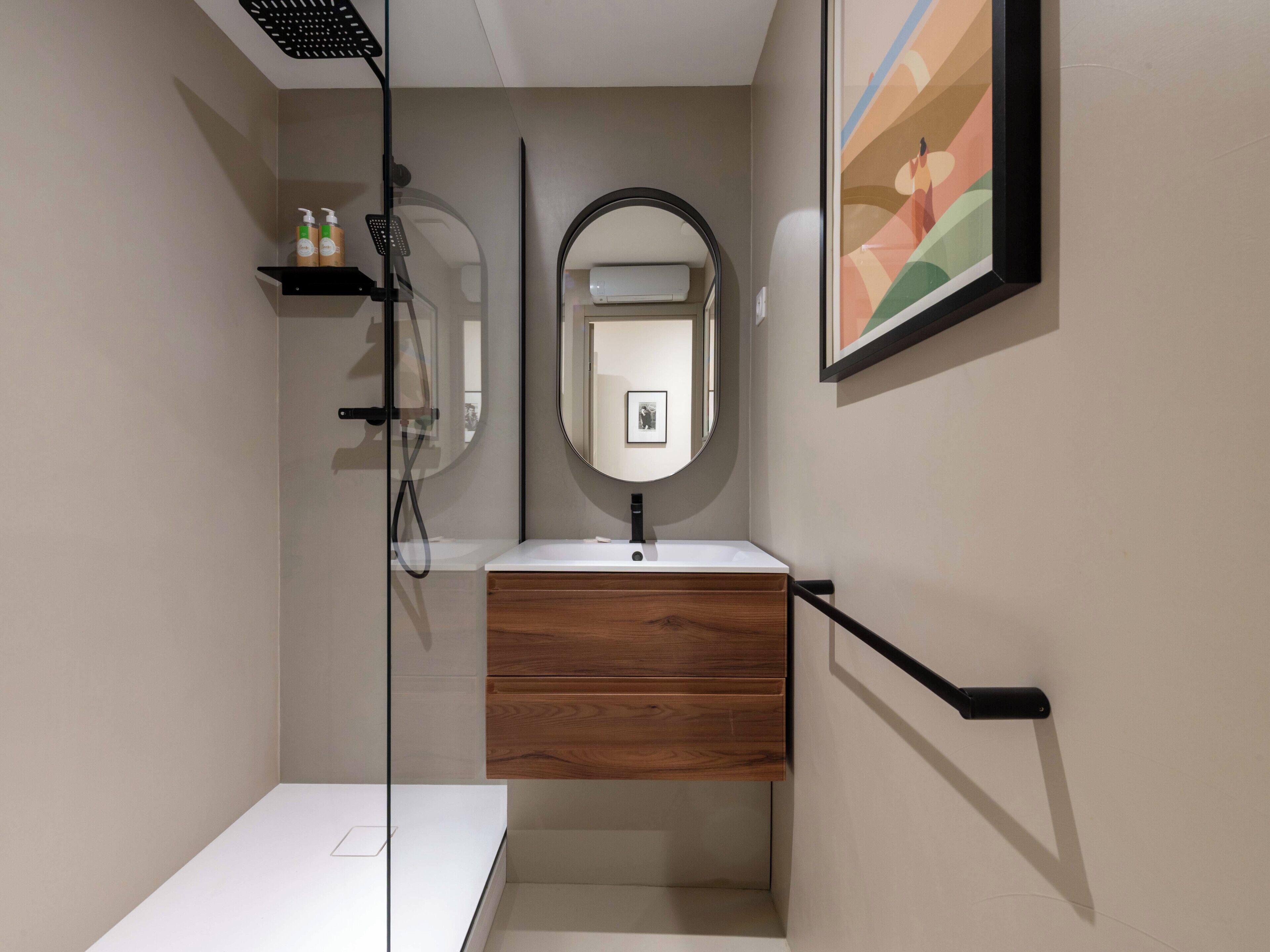 Une salle de bain moderne avec une douche à parois de verre, un meuble-lavabo en bois, un lavabo blanc et un tableau encadré au mur.