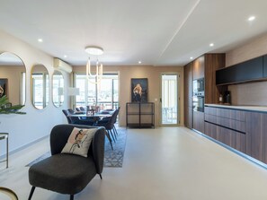 A modern living room with a dining area, a kitchen with a built-in oven, and a large window offering a view. - 2-Br Apartment – Terrace, Cannes City Centre (Cannes)