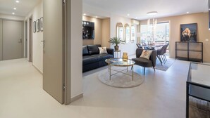 Un salon moderne comprenant un canapé, des fauteuils, une table basse et un coin repas avec des chaises.