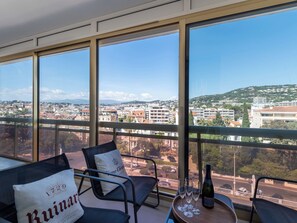 A balcony with a view of a cityscape, a bottle of champagne, and two chairs with cushions. - 2-Br Apartment – Terrace, Cannes City Centre (Cannes)