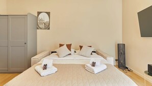 A hotel room with a bed, pillows, a bedside table, a TV, and a wardrobe. - Bright Cosy Suite Paris 16th Steps From Seine (Paris)