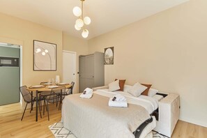 A hotel room with a bed, bedside tables, a desk with chairs, a microwave, and a door. - Bright Cosy Suite Paris 16th Steps From Seine (Paris)