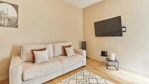 A living room with a sofa, a flat-screen TV, a small table with a vase, and a picture frame on the wall. - Bright Cosy Suite Paris 16th Steps From Seine (Paris)