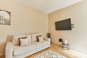 A living room with a sofa, a flat-screen TV, a small table with a vase, and a picture frame on the wall. - Bright Cosy Suite Paris 16th Steps From Seine (Paris)