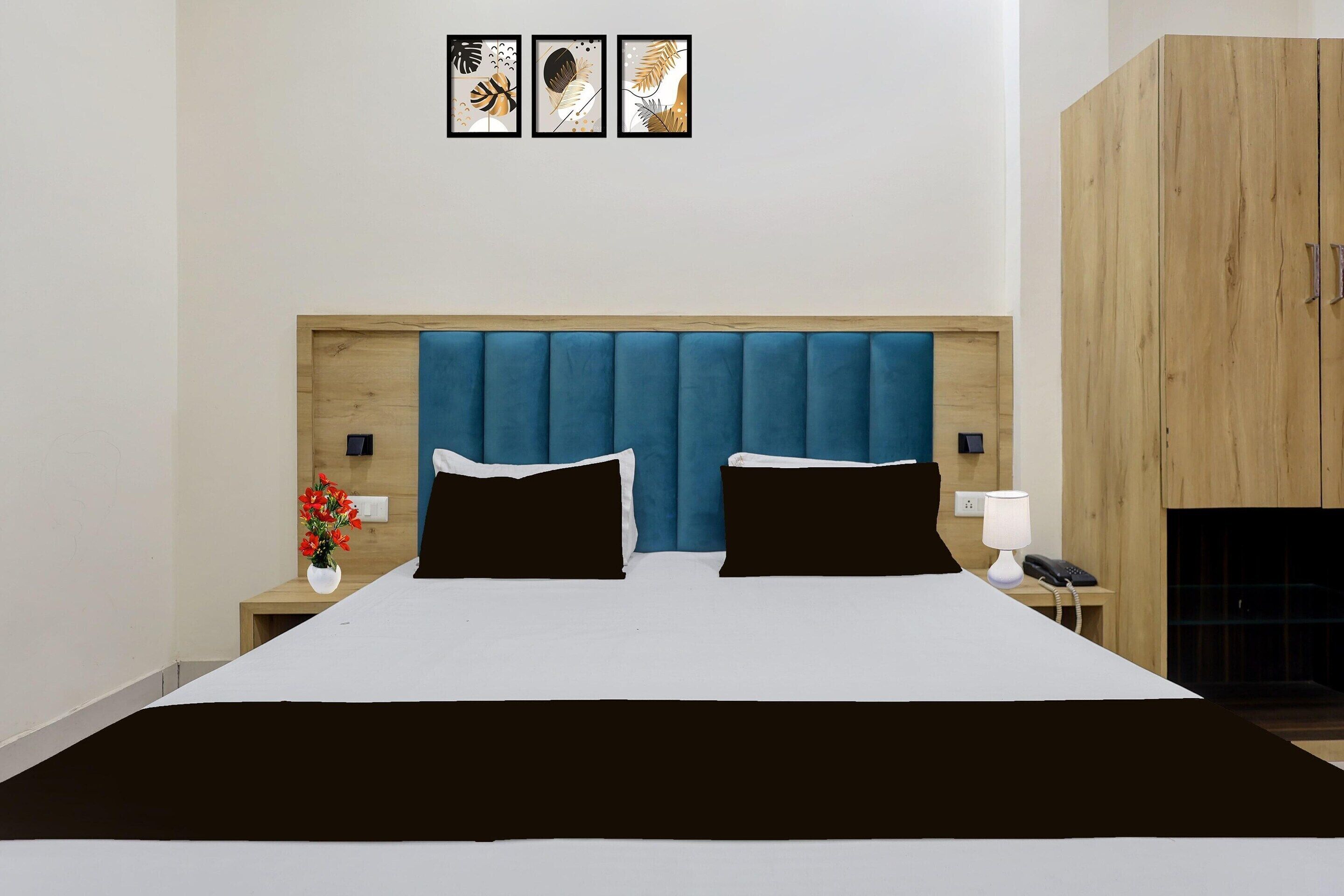A hotel room with a bed, a nightstand with a lamp, a vase with flowers, and a wooden wardrobe.
