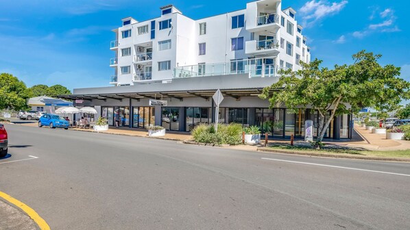 A multi-story hotel with a covered outdoor seating area, a visible entrance, and a clear sky.