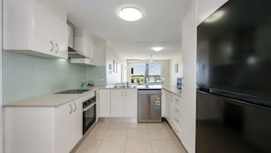A modern kitchen with white cabinets, a stainless steel refrigerator, and a dishwasher. - Platinum Apartments -  Unit 22 (Bargara)