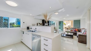 A modern kitchen with white cabinetry, a dishwasher, and a dining area with a sofa and a coffee table. - Dual Living, Pool, Gym, Sleeps 8, Parking (Bargara)