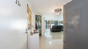 A hallway with a white wall, a door labeled '3B', a decorative wall with a waterfall mural, a chandelier, and a glimpse of a living room with a sofa. - Dual Living, Pool, Gym, Sleeps 8, Parking (Bargara)
