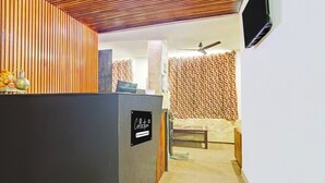 A reception area with a wooden slatted ceiling, a reception desk, a sofa, and a television mounted on the wall.