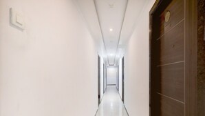 A long, narrow hallway with white walls and a tiled floor, leading to a door with a dark panel. - Saver Double Hotel Admire Suit (Chennai)