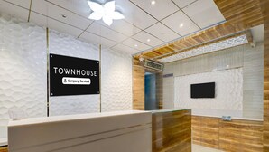 A reception area with a sign reading 'TOWNHOUSE Company-Serviced,' a modern design with a wooden accent wall, and a mounted television. - Saver Double Hotel Admire Suit (Chennai)