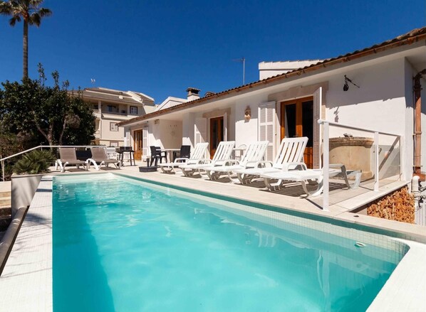 A swimming pool with lounge chairs and a table, surrounded by white buildings with balconies.