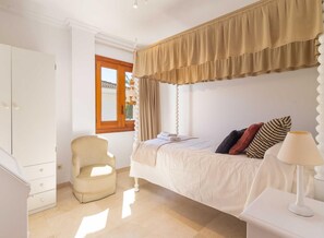 Une chambre à coucher avec un lit, une chaise, une lampe, une armoire et une fenêtre.