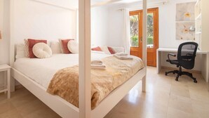 Una cama con dosel, un escritorio con silla y vistas a la vegetación a través de una puerta.