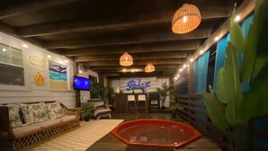 A cozy indoor space with a wooden deck, a red hot tub, a sofa with a tropical print, and a reception desk.