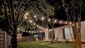 A backyard with artificial lighting, a lawn, and a white building.