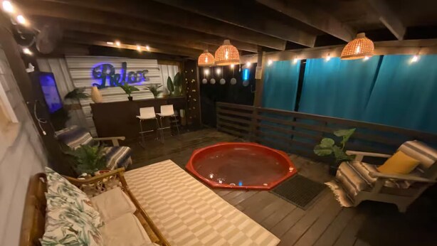 A wooden deck with a pool, lounge chairs, a sofa, and a bar area with a neon sign.