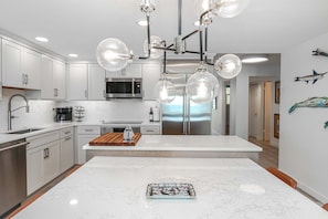 A modern kitchen with white cabinetry, a central island, and a stainless steel refrigerator. - Sand Dollar 3-305: Direct Oceanfront 3/2 Condo, Luxury in St. Augustine Beach! (St. Augustine)