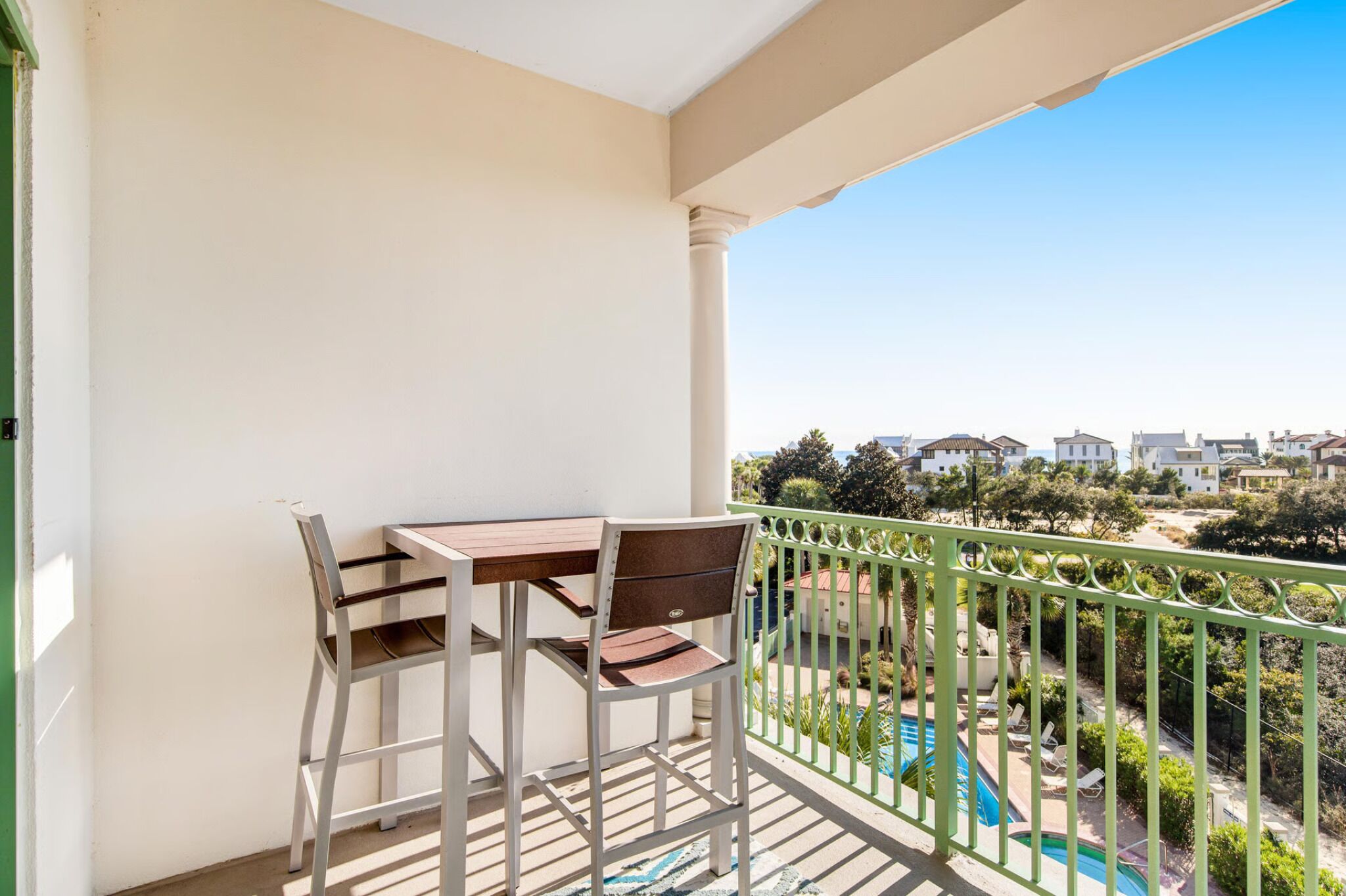 Een balkon met een tafel en stoelen, een zwembad en uitzicht op huizen en groen.