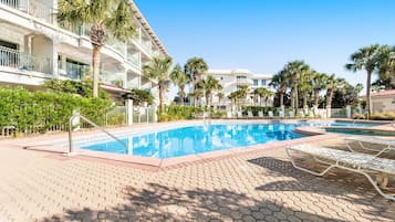 Ein Hotelpoolbereich mit klarem, blauem Pool, Liegestühlen, Palmen und einem mehrstöckigen Gebäude mit Balkonen.