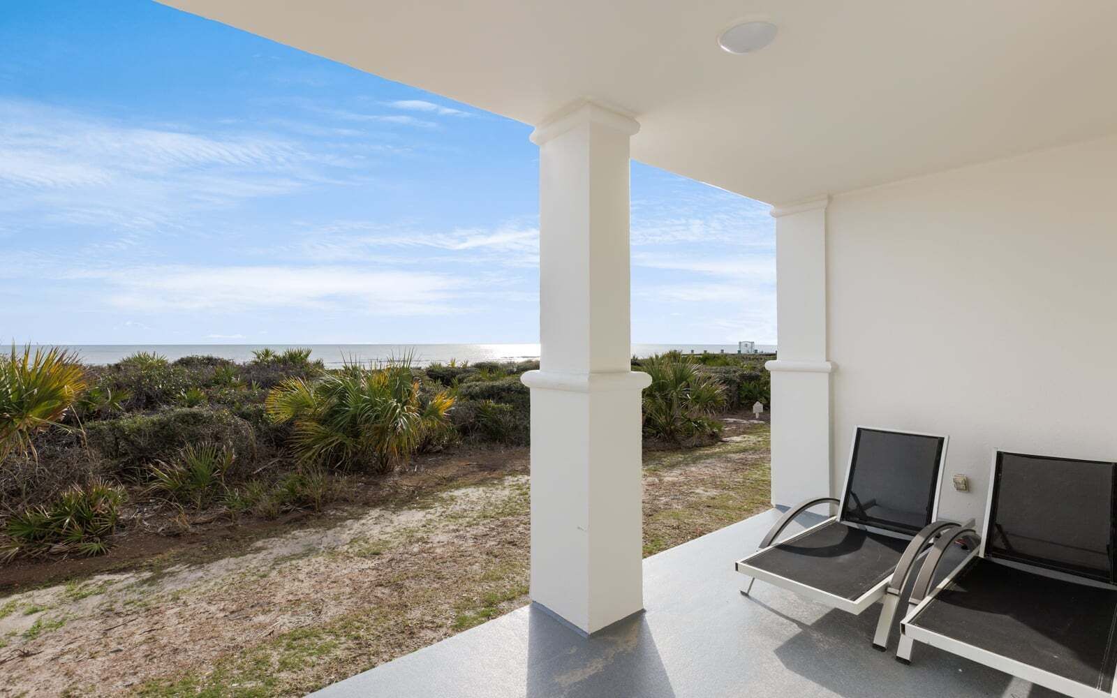 A covered outdoor area with two chairs, a view of the beach, and a white building structure.