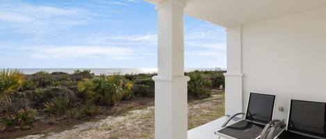 A covered outdoor area with two chairs, a view of the beach, and a white building structure.